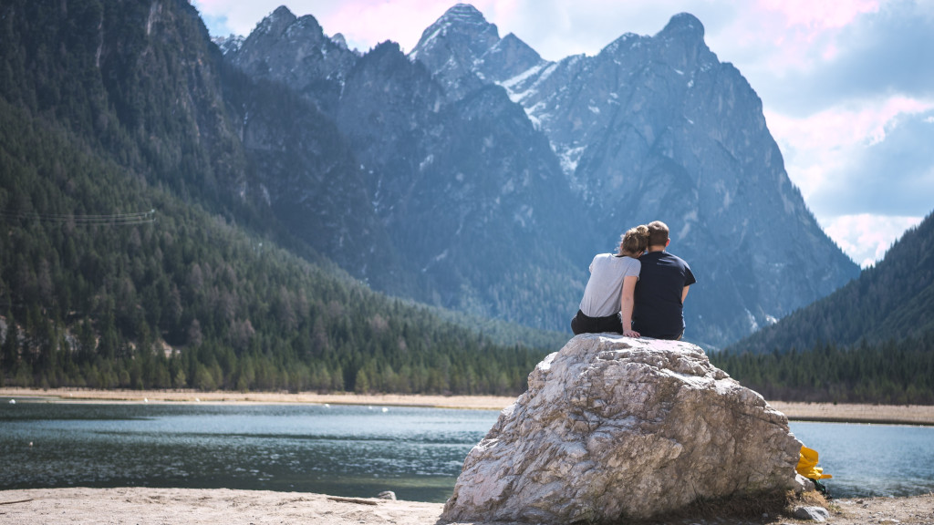 pareja en una roca frente a una montaña y el mar